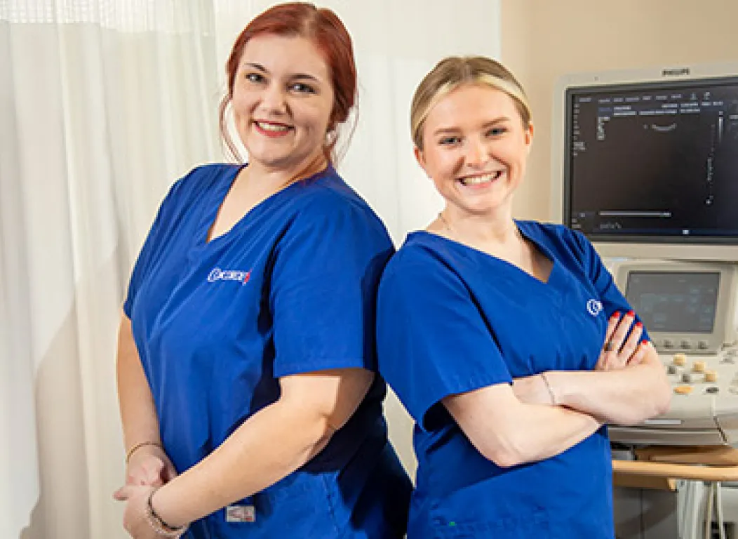 Two female graduates from Concorde's Diagnostic Medical Sonography Program in blue scrubs smiling.