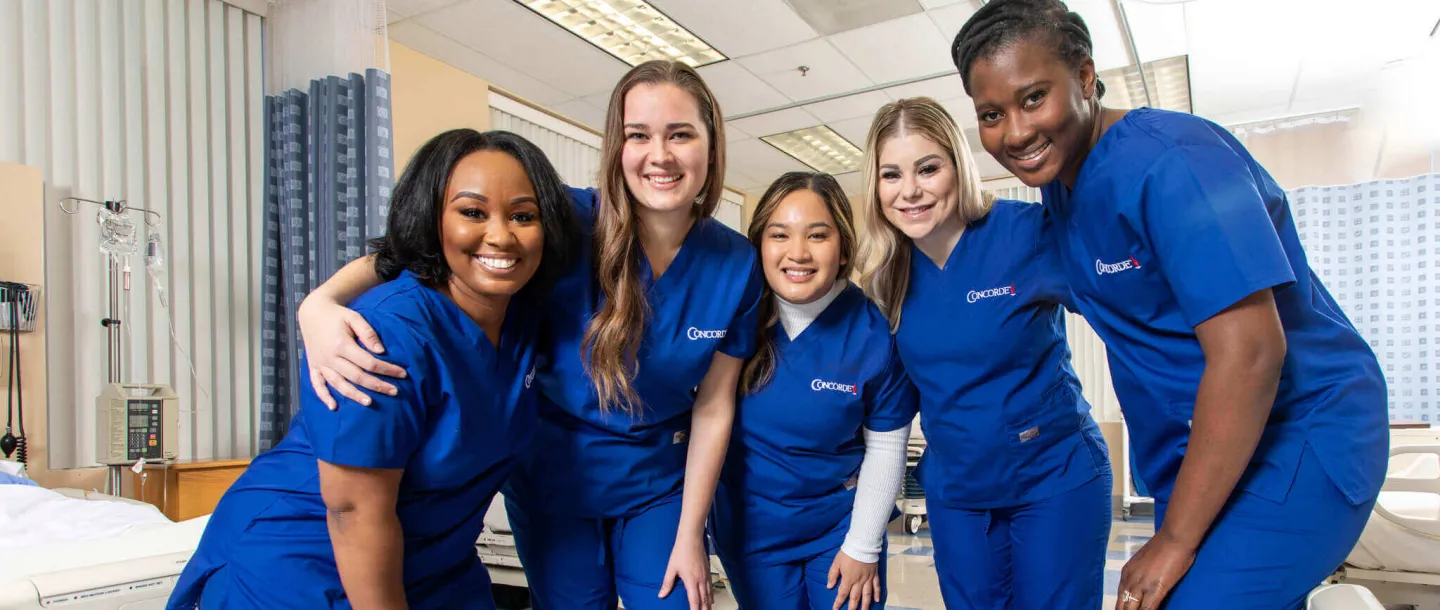 5 smiling Concorde graduates in blue scrubs in lab setting