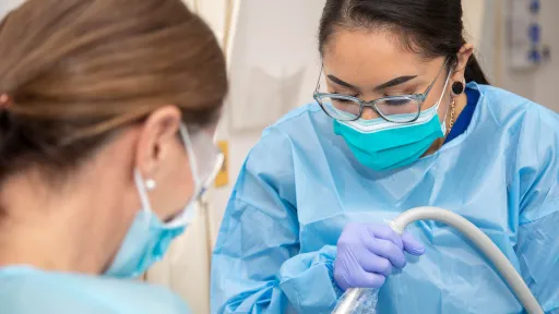 Lindsay in a dental gown providing dental evacuation under the supervision of an instructor.
