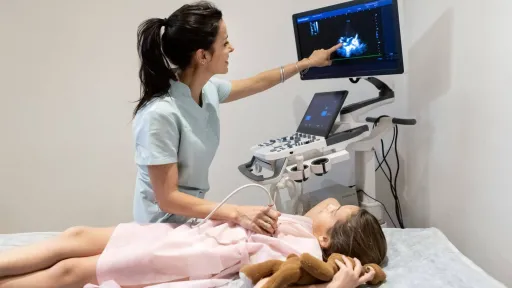 Echocardiogram technician performing heart ultrasound on child and reviewing cardiac images on screen during exam.
