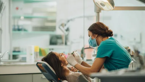 Dental hygienist wearing teal scrubs performing a teeth cleaning on a female patient in a dental office
