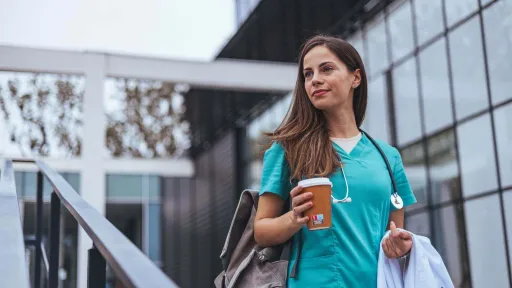 Travel nurse in scrubs holding coffee and walking outside a modern building, capturing the flexibility and independence of a travel nursing career