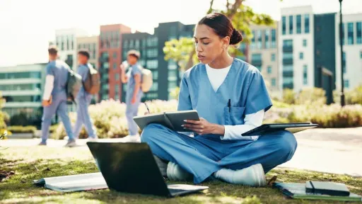 A nursing student sitting in a courtyard, focusing on digital coursework.