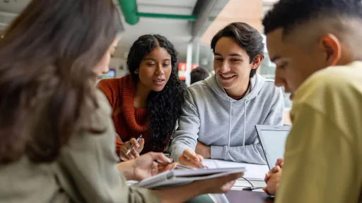 A group of diverse students sitting together at a table, discussing notes and reviewing materials to help each other pass their exams.