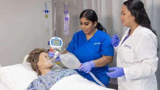 A female nurse in blue scrubs works with patient dummy while doctor supervises