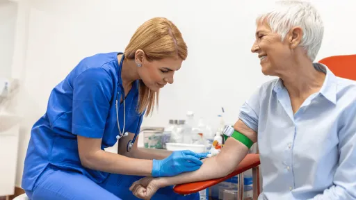 Female phlebotomist with blonde hair draws blood from elderly patient's arm