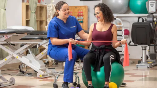 A female physical therapist assistant in blue scrubs assists a female patient with exercises