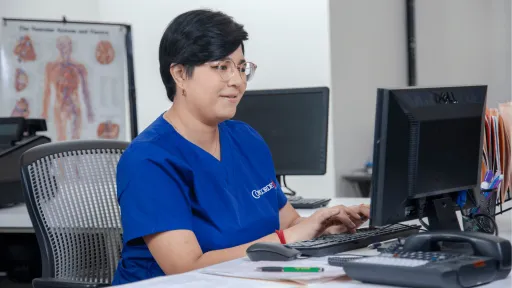 female medical office administrator in blue scrubs works at computer in medical office