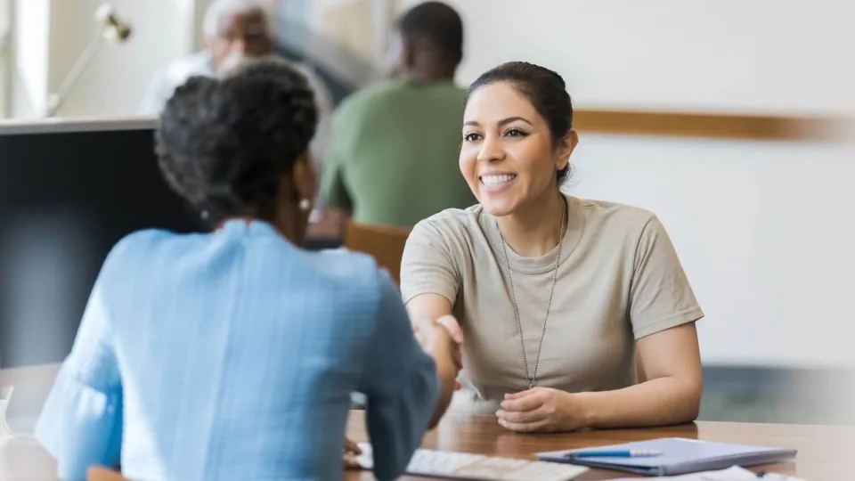 A smiling female service member in uniform shaking hands with a career counselor during a meeting to discuss using military tuition assistance for vocational training and career advancement.