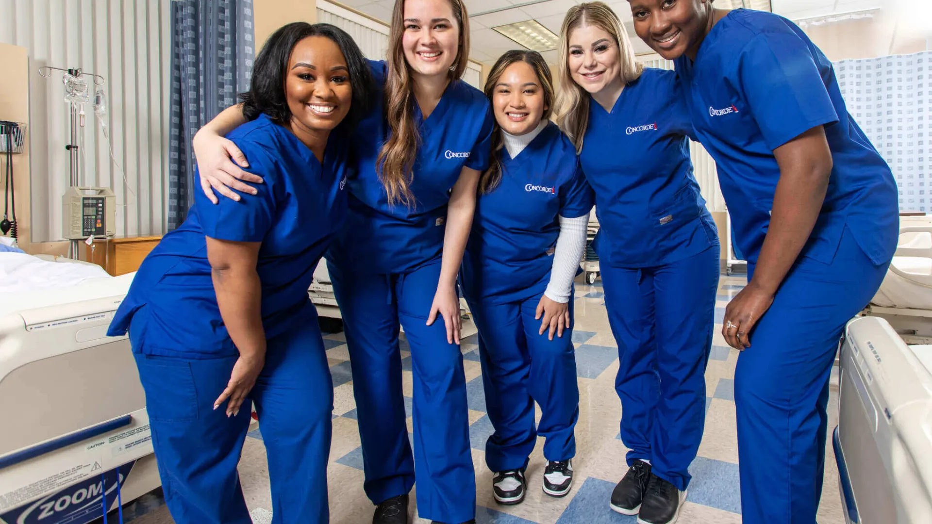 5 smiling Concorde graduates in blue scrubs in lab setting
