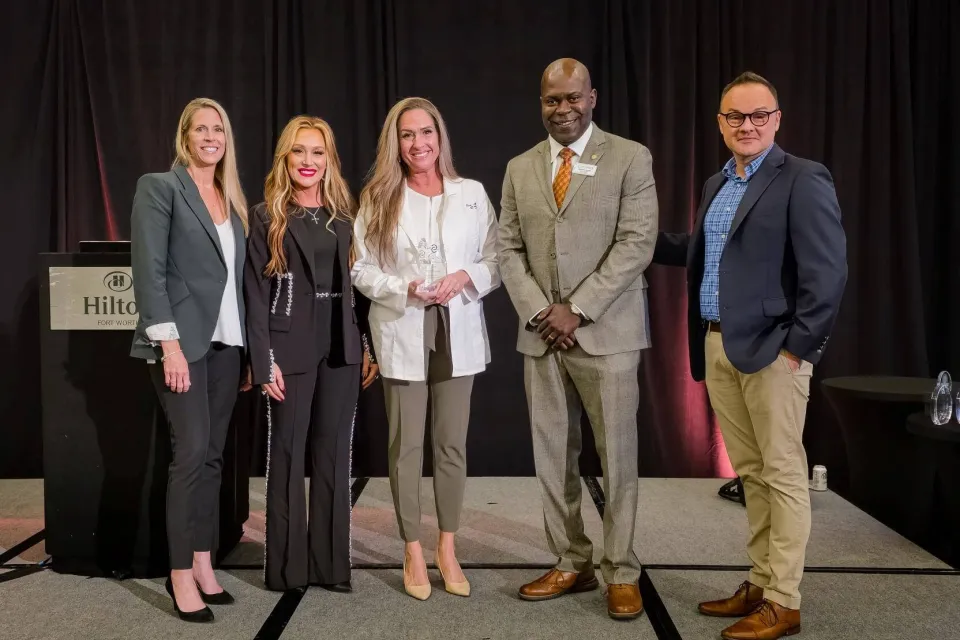 Group photo of five individuals in business attire on stage during a Graduate of the Year presentation