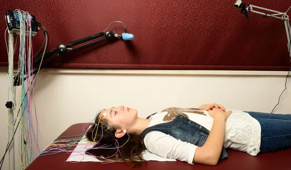 A female sleep study patient connected to EEG equipment sleeps on an examination table in a medical office during a sleep study.