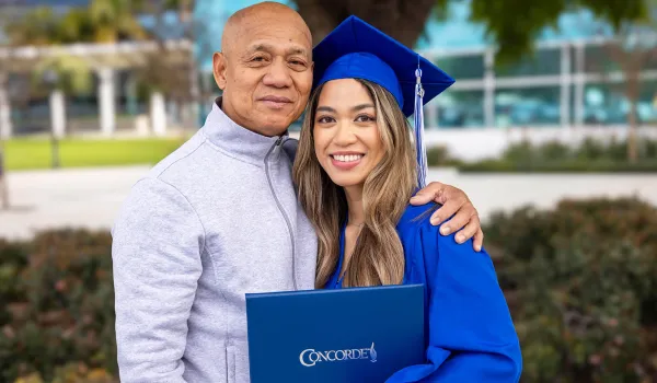 Concorde graduate wearing cap and gown holds degree and poses with proud family member.