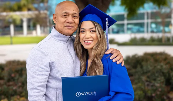 Concorde graduate wearing cap and gown holds degree and poses with proud family member.