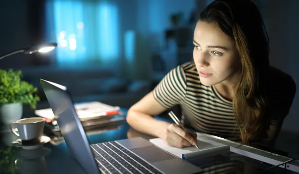 Young working woman studying for class on the computer at night.