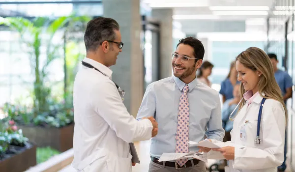 Healthcare Administrator holding papers shakes hands with a doctor in a hospital