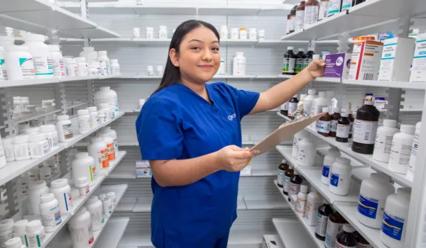Pharmacy technician organizing medication on shelves with a clipboard.