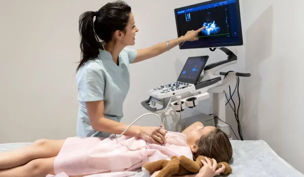 Echocardiogram technician performing heart ultrasound on child and reviewing cardiac images on screen during exam.