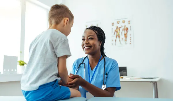 Smiling medical assistant supports young patient during checkup in clinical exam room setting.