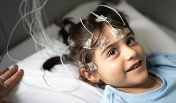 Smiling child with electrodes attached during a sleep study, representing the role of a polysomnographer in monitoring pediatric sleep patterns