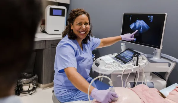 Smiling healthcare professional in scrubs performing an ultrasound scan and pointing to the fetal image on the monitor