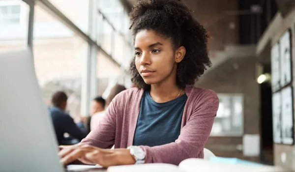 A focused young woman using a laptop in a bright study area to research FAFSA deadlines and submit her financial aid application online.