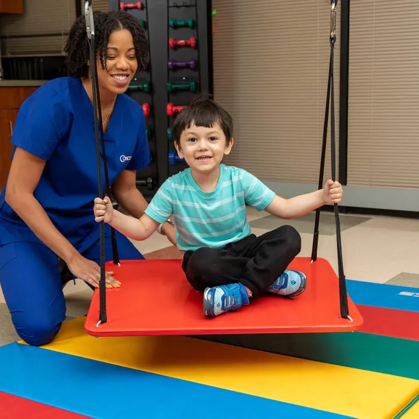 Occupational Therapist Assistant and young boy on swing demonstrating therapy for Occupational Therapy Month