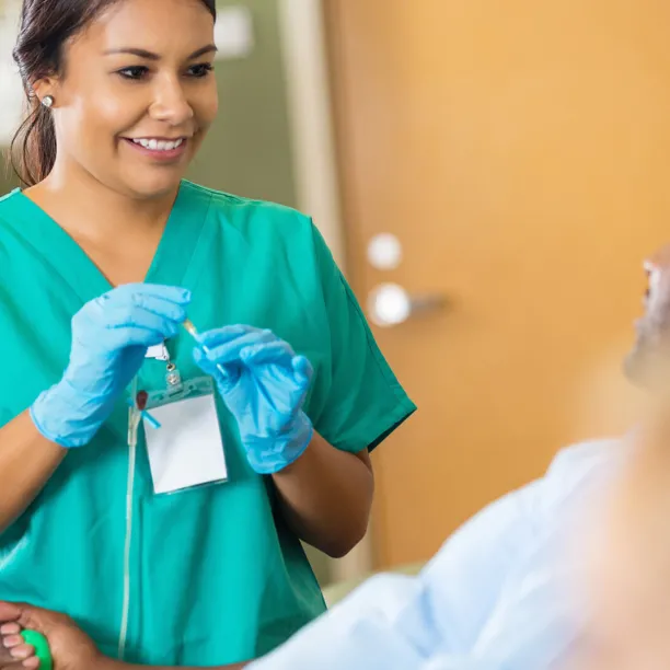 Phlebotomy Technician holding a needle soothes male patient about to give blood.