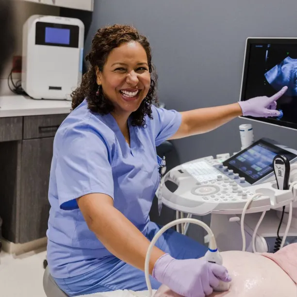 Smiling healthcare professional in scrubs performing an ultrasound scan and pointing to the fetal image on the monitor