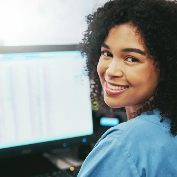 Smiling woman in blue scrubs working at a computer, representing Medical Office Administration Certificate Program skills.