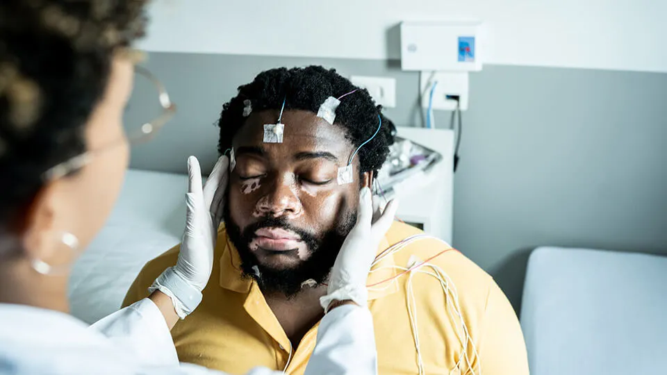 A polysomnographic technologist places electrodes on a patient's head to prepare him for a sleep study. A polysomnographic technologist places electrodes on a patient's head to prepare him for a sleep study.