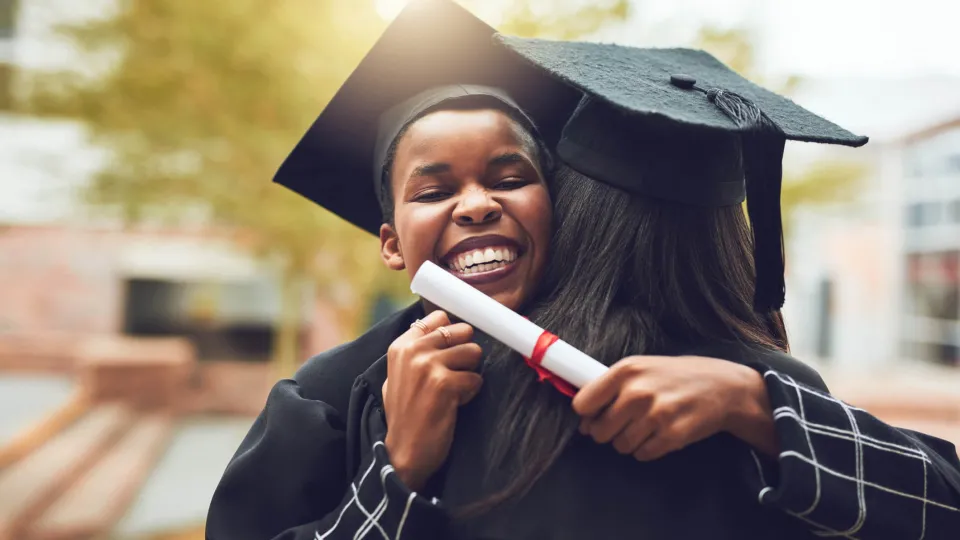 Graduate in cap and gown getting a celebratory hug.