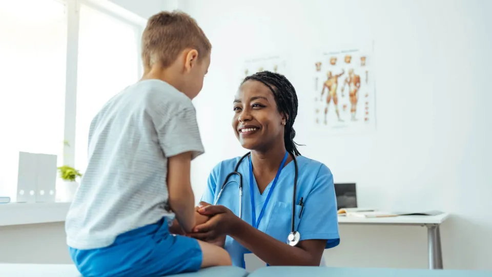 Smiling medical assistant supports young patient during checkup in clinical exam room setting Smiling medical assistant supports young patient during checkup in clinical exam room setting.