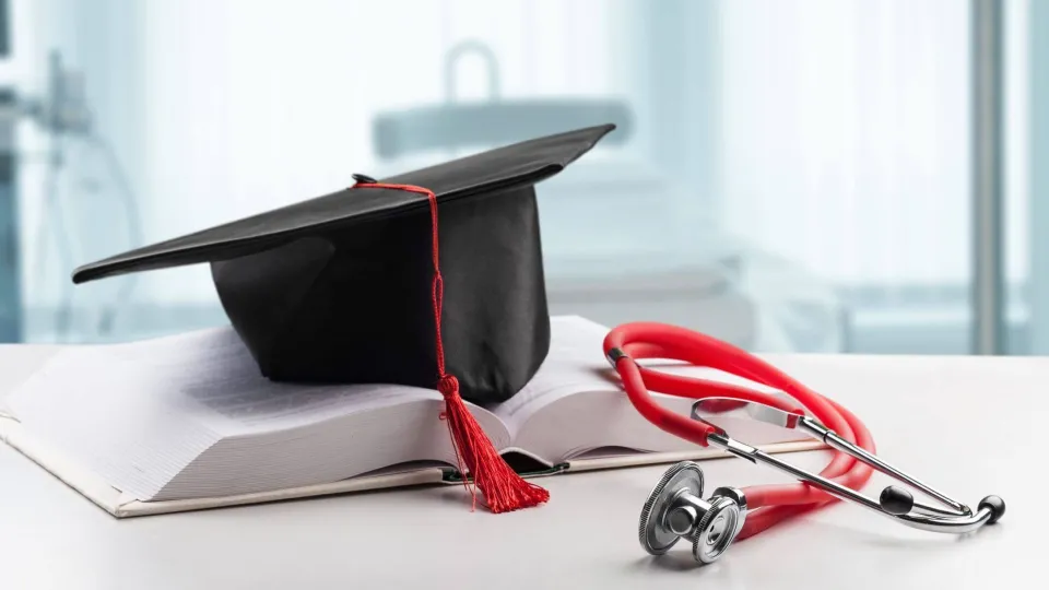 Graduation cap and stethoscope resting on an open medical textbook, representing education and career paths in health administration.