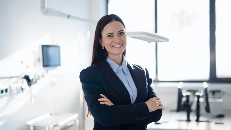 Professional woman in a business suit standing confidently in a medical office, symbolizing leadership in health care administration.