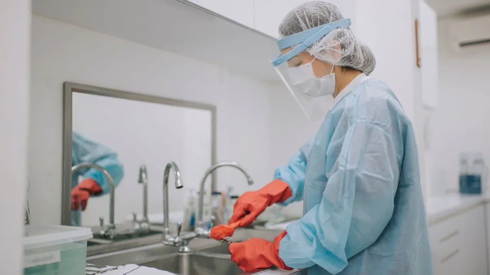 Sterile processing technician cleaning surgical tools at a sink, representing job responsibilities and outlook Sterile processing technician cleaning surgical tools at a sink, representing job responsibilities and outlook