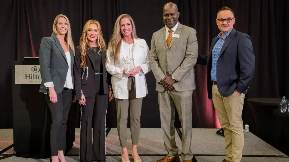 Group photo of five individuals in business attire on stage during a Graduate of the Year presentation