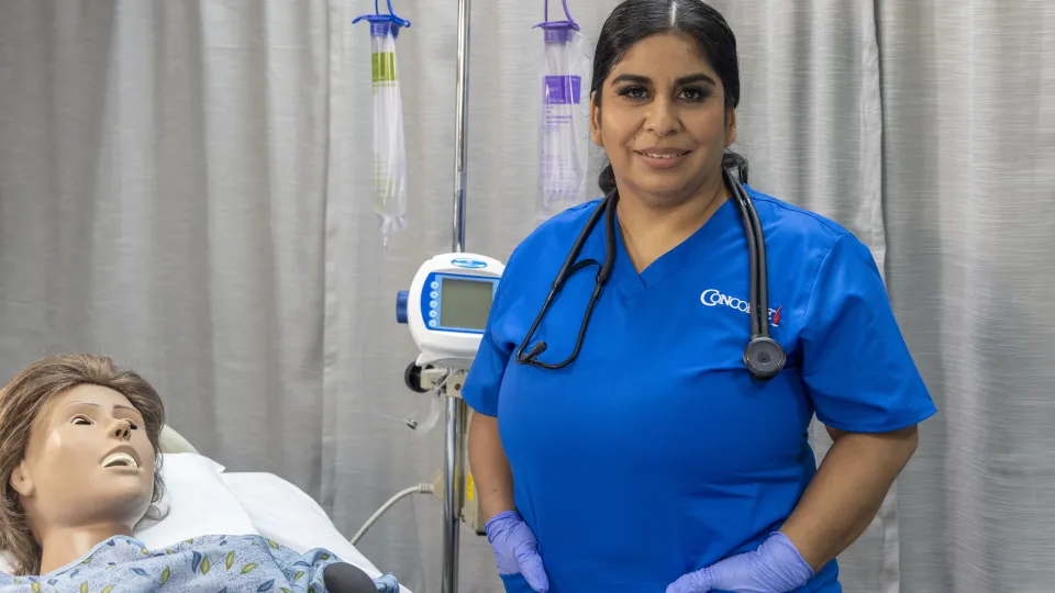 A female nurse with dark hair and blue scrubs poses for camera in lab setting