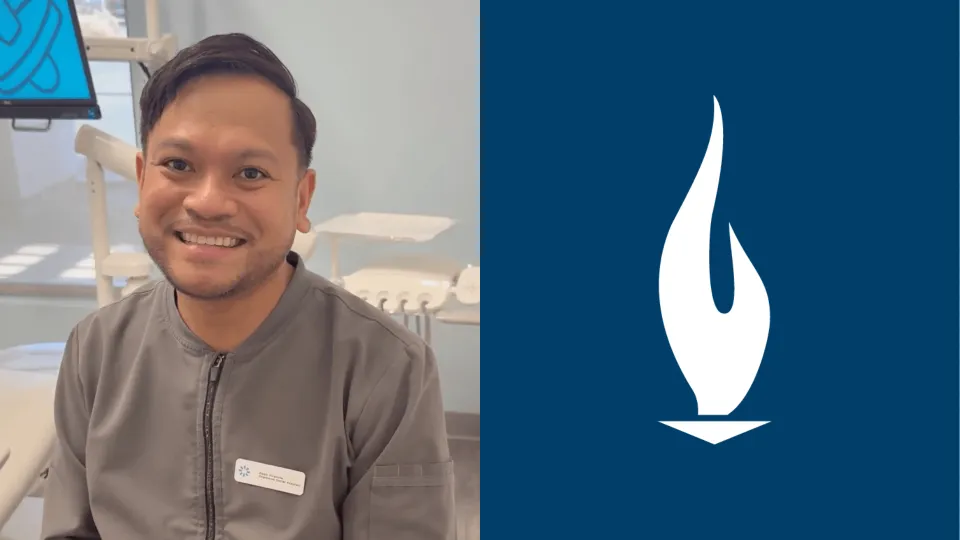 A male dental assistant with brown hair and wearing grey scrubs smiles for camera