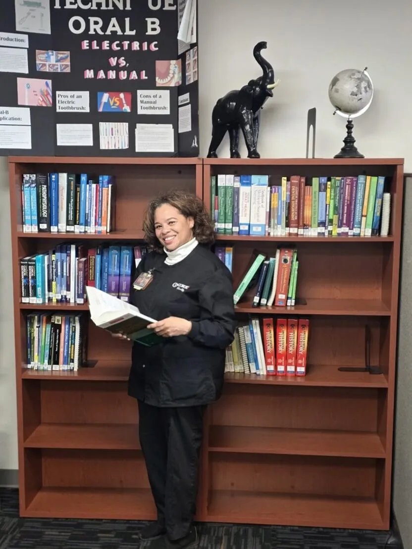 Selinza in her black Concorde scrubs reading a book in Grand Prairie's Learning Resource Center.
